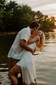 a man and woman are hugging in the water at sunset, with trees in the background