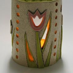 a ceramic vase with an orange flower and green stems on it's side, sitting on a white surface