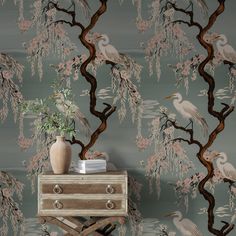 a wallpaper with birds and flowers on it, next to a small chest of drawers