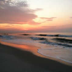 the sun is setting over the ocean with waves coming in