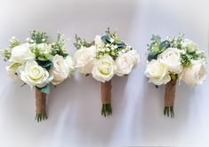 three bouquets of white roses and greenery are lined up on the wall next to each other