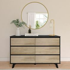 a black and white dresser with a round mirror above it, next to a potted plant