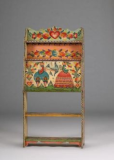 an ornately decorated wooden shelf with painted designs on the top and bottom, against a gray background