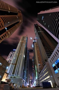 some very tall buildings at night time with lights on and clouds in the sky above them