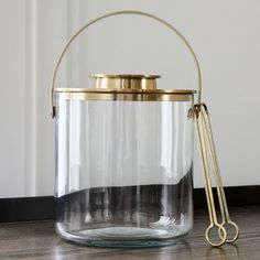 a clear glass container with gold handles and a pair of scissors sitting on the floor