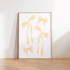 a white frame with yellow bows hanging on the wall next to a wooden floor and hardwood floor