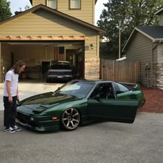 a man standing next to a green car in front of a house with a garage door open