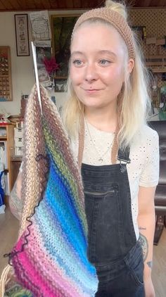 a woman with blonde hair holding up a multicolored knitted piece of cloth