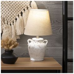 a white vase sitting on top of a wooden table next to a lampshade