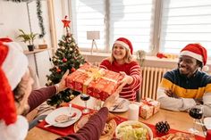 group of people sitting around a table with food and presents on it, all dressed up for christmas