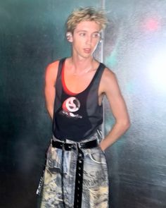 a young man standing in front of a metal wall wearing a tank top and shorts