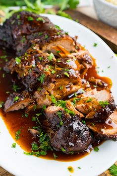 a white plate topped with meat covered in sauce and garnished with parsley