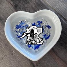 a heart shaped bowl filled with blue and white confetti on top of a wooden table