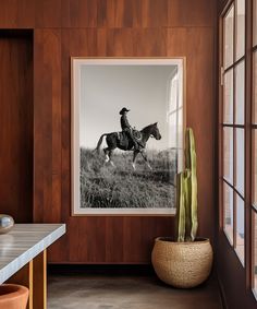 a black and white photo of a man on a horse in a field near a window