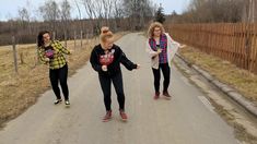 three women are walking down the road with one pointing at something in her hand while another looks on