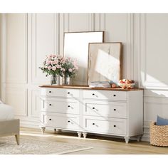 a white dresser with flowers on top and a mirror above it in a bedroom setting