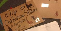 two cardboard signs with horses on them sitting on the floor next to some papers that read a trip to chickasaw stables