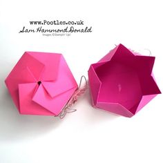 two origami umbrellas sitting side by side on top of each other in pink paper