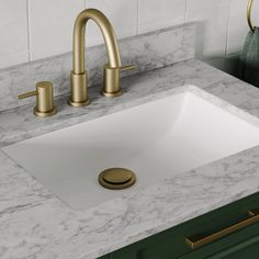 a bathroom sink with gold faucet and marble counter top next to green cabinets