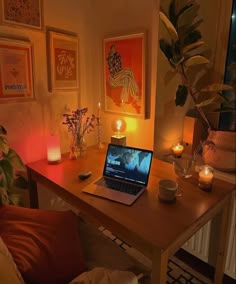 a laptop computer sitting on top of a wooden desk next to a candle and potted plant