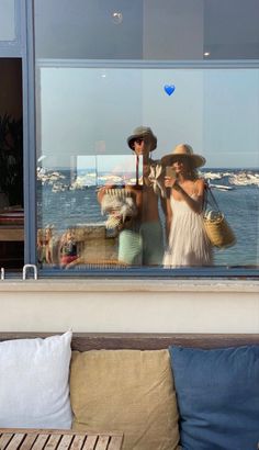 two women are reflected in the window of a house on the beach, while another woman is holding a basket