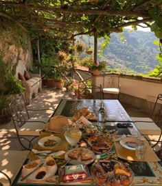 an outdoor table with food and drinks on it under a pergolated roof over looking the mountains