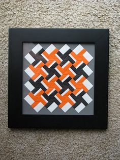 an orange and black square pattern in a frame on the wall next to a carpet