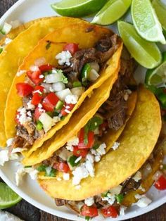 three tacos on a white plate with limes