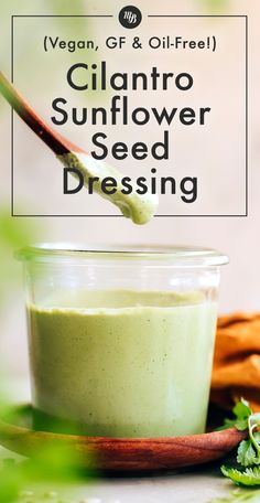 a glass jar filled with green sunflower seed dressing on top of a wooden spoon