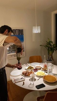 a man is pouring something into a glass on a table with food and drinks around it