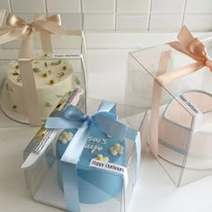 three small cakes in clear boxes with bows and ribbons on the top one is blue