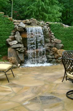 a small waterfall in the middle of a stone patio with chairs and tables around it