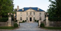 a large white house with blue roof surrounded by greenery and stone pillars on either side of the driveway