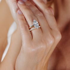 a woman holding her hand up to her face with two engagement rings on her fingers