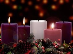 three lit candles surrounded by holly and pine cones