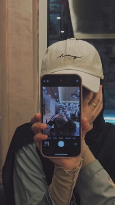 a person taking a selfie with their cell phone in front of them, wearing a hat