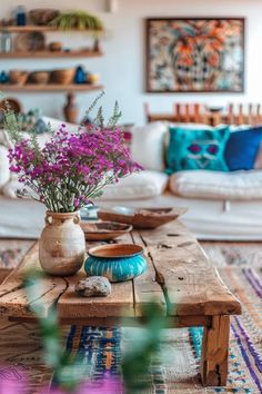 a wooden table topped with purple flowers on top of a blue and white rug next to a couch