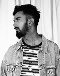 a man with a beard wearing a denim jacket and striped t - shirt looks off to the side