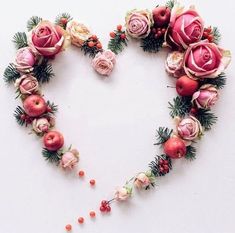 a heart made out of flowers and apples on a white surface with berries scattered around it