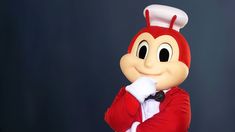 a person in a red suit with a white hat and bow tie standing next to a black background