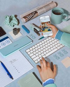 a person using a cell phone while sitting at a desk with various items on it