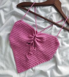 a pink knitted heart hanging on a wooden hanger next to a white sheet