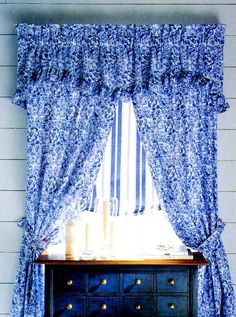 a blue dresser sitting under a window next to a white wall with curtains on it