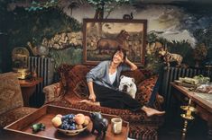 an older woman sitting on a couch with her dog in front of a wall painting