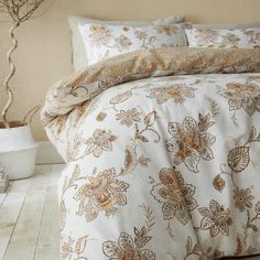 a bed with white and gold comforters in a room next to a vase filled with flowers