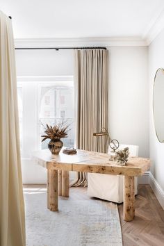 a living room with white walls and wooden furniture in front of a large window that has drapes