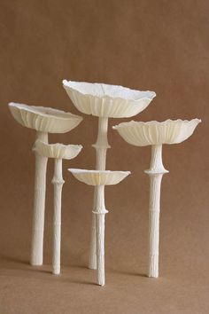 four white vases are lined up against a brown background, one is made out of paper