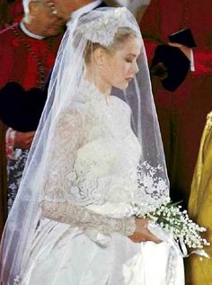 the bride is walking down the aisle in her wedding dress and veil with flowers on it