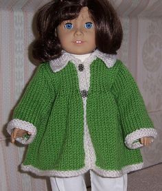 a doll wearing a green coat and white pants with blue eyes is standing in front of a couch