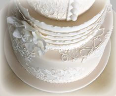 a three tiered cake with white frosting and flowers on the top, sitting on a plate